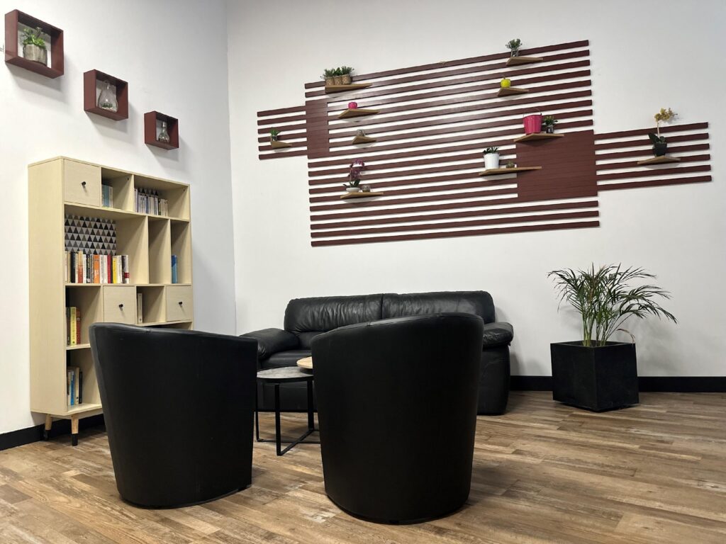 Coin Détente Bureau : Mobilier Noir et Déco Moderne Coin détente moderne avec canapé et fauteuils noirs en cuir, étagères murales marron à lattes, bibliothèque claire et plantes.