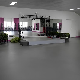 Salle Fitness Aérobic Miroir Scène Équipements Salle de fitness moderne avec plancher gris, grand miroir, scène d'aérobic avec marches empilées, vélos d'appartement visibles à travers les reflets.