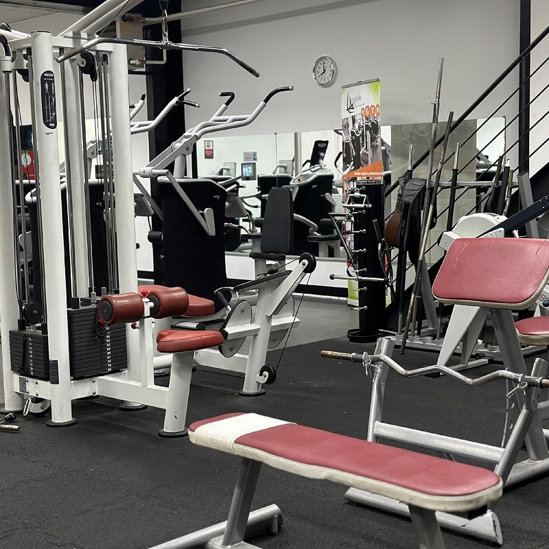 Machines de musculation et bancs rouges en salle de sport Intérieur d'une salle de sport avec des machines de musculation blanches et rouges, un banc plat, et un miroir réfléchissant d'autres équipements.